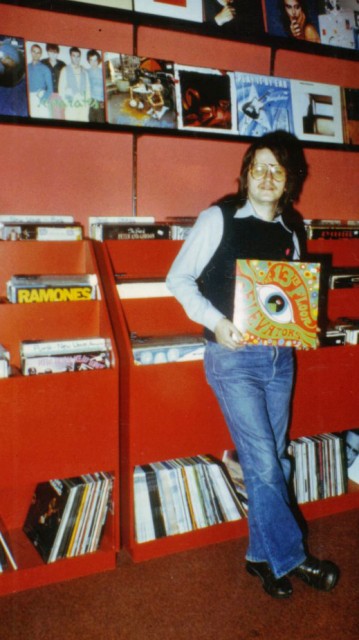 En mann i 1978-klær med en klassisk psykedeliaplate i hånden. Han står foran en platehylle.