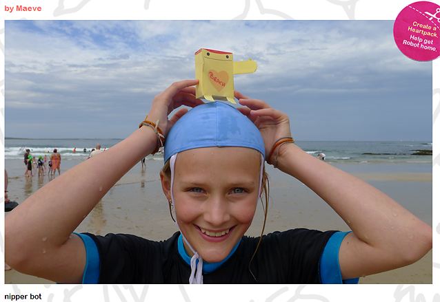 en smilende jente på en strand i badetøy og badehette. Oppå hodet sitt holder hun en papirrobot med teksten "beach" inni et hjerte.