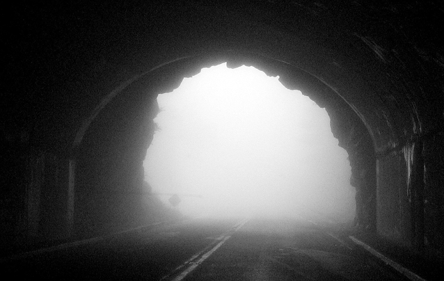 Svarthvittfotografi av en tunellåpning sett innenfra med lys tåke utenfor.