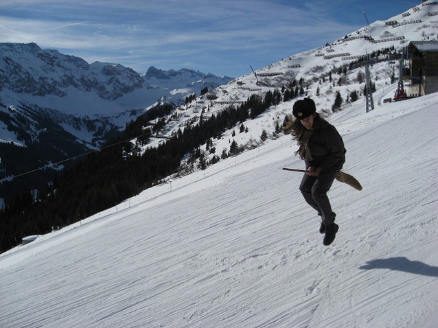 en jente som holder en sopelime mellom bena, i svevet 10 cm over bakken i en slalombakke