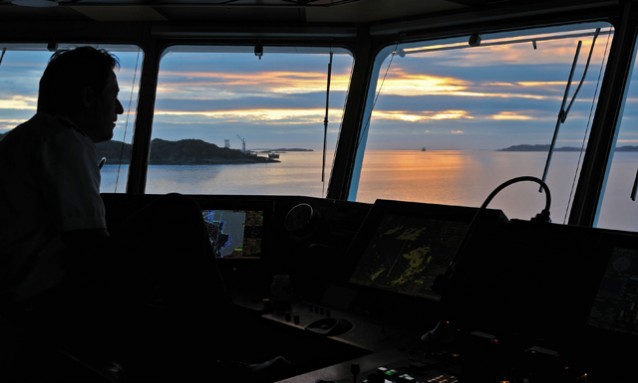 low sun outside the bridge window of Hurtigruten, the silhoutte of a man controlling the boat is visible