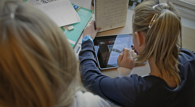 To jenter sitter ved siden av hverandre og arbeider på en iPad