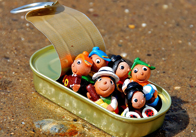Foto av en samling smilende lekefigurer som sitter i en sardinboks på en strand