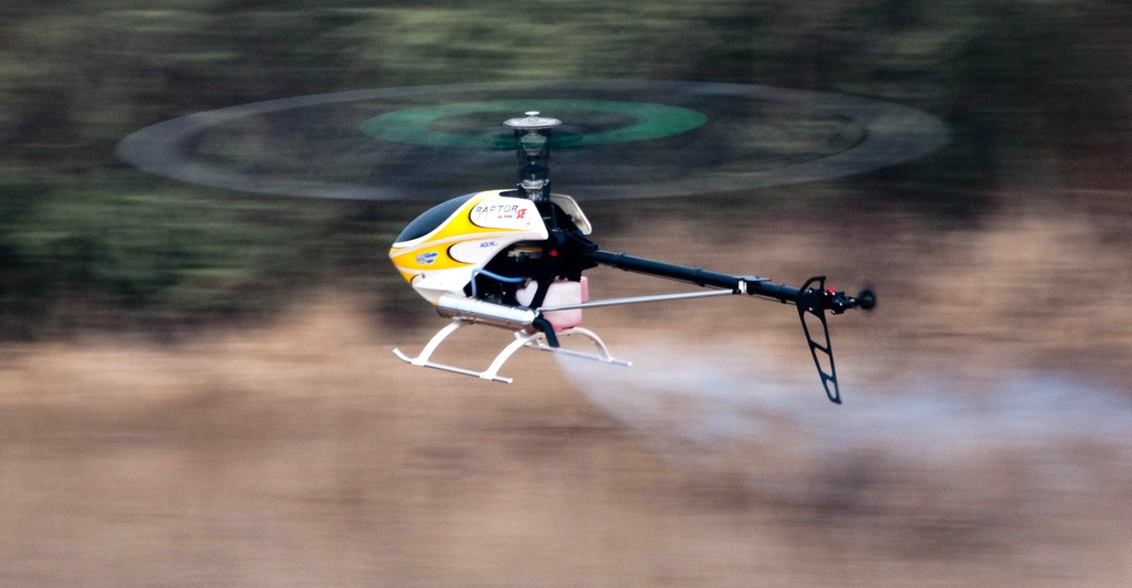 Modellhelikopter i flukt foran en skog