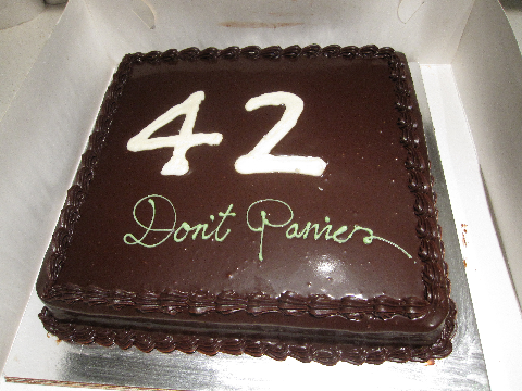 foto av en kvadratisk sjokoladekake med tallet 42 i store glasurbokstaver og teksten Don't Panic i grønn handwriting