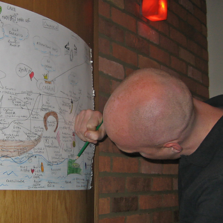 En mann fargelegger noe grønt på et kart som henger på en vegg. Over hodet hans, et studio-rødlys
