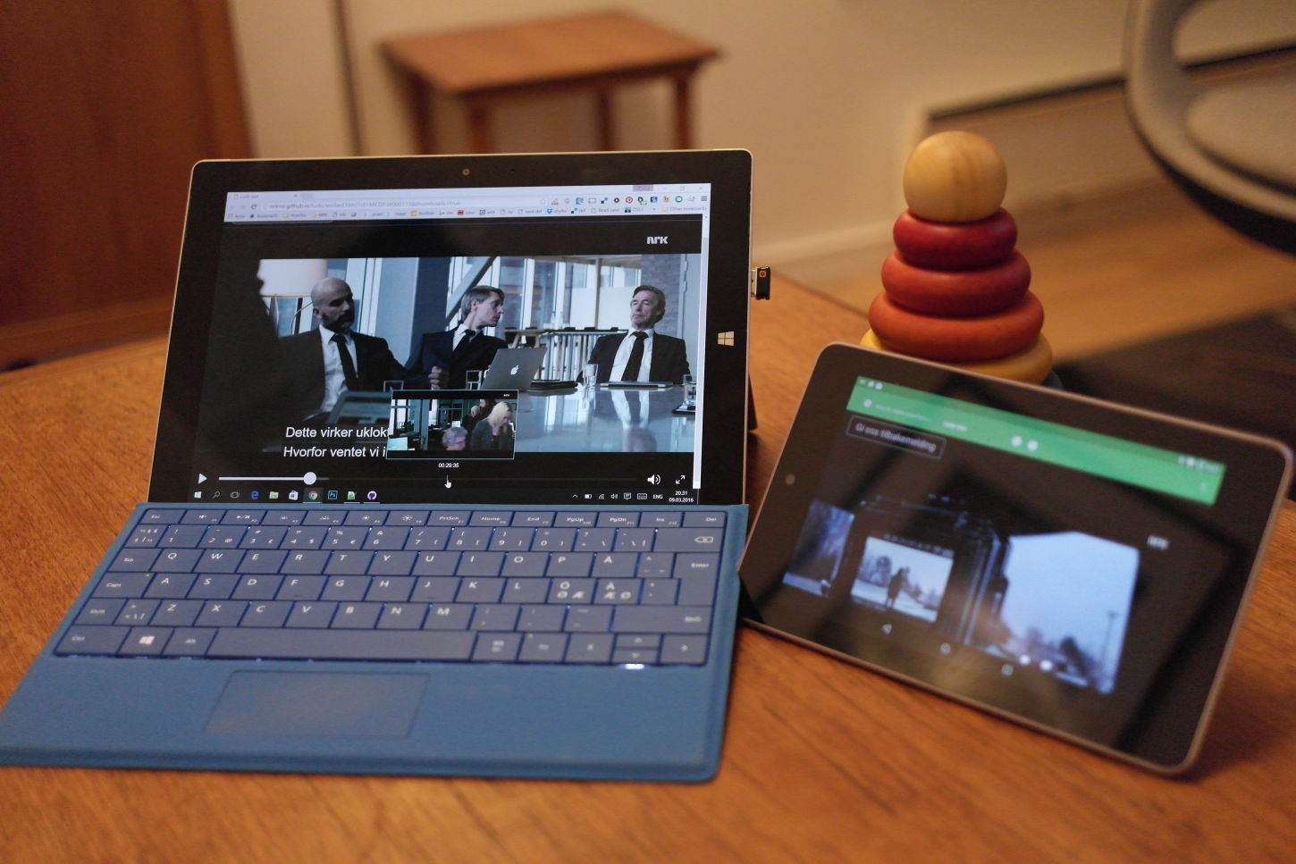 NRKs nye avspiller på Google Nexus 7 og Microsoft Surface avbildet på et hipster teakbord, med stabletårn i tre brukt som støtte.
