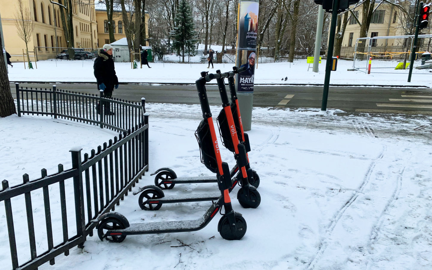 Tre elektriske sparkesykler står oppstillt et sted i Oslo, og det er snø på bakken.