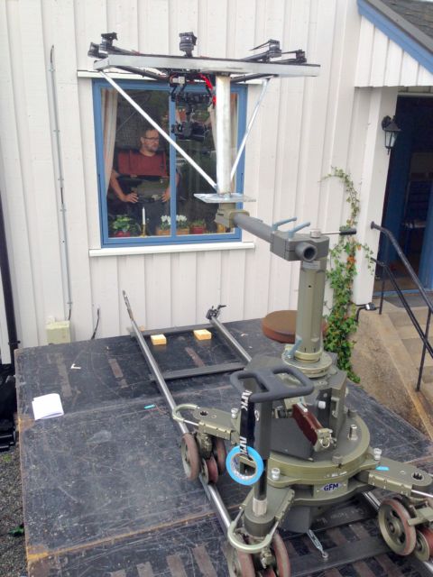 Bildet viser en stor drone montert på en kamerakran. Dronen og kranen peker inn mot et vindu på et bolighus. 