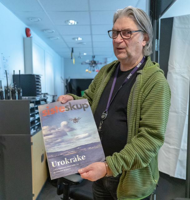 Reidar Otto Johnsen holder opp et blad med tittelen «Siste skup», hvor hovedoppslaget er «Urokråke» - «Luftfartøyet som setter etikk, jus og sikkerhet på prøve».