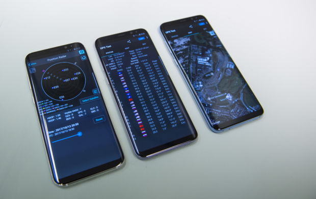 Tre mobiltelefoner ligger ved siden av hverandre og viser ulike skjermer med satellittinformasjon. Den nærmeste en visualisering av jordkloden med punkter som representerer satellitter, de andre viser tabeller og andre data fra det som ser ut som samme app.