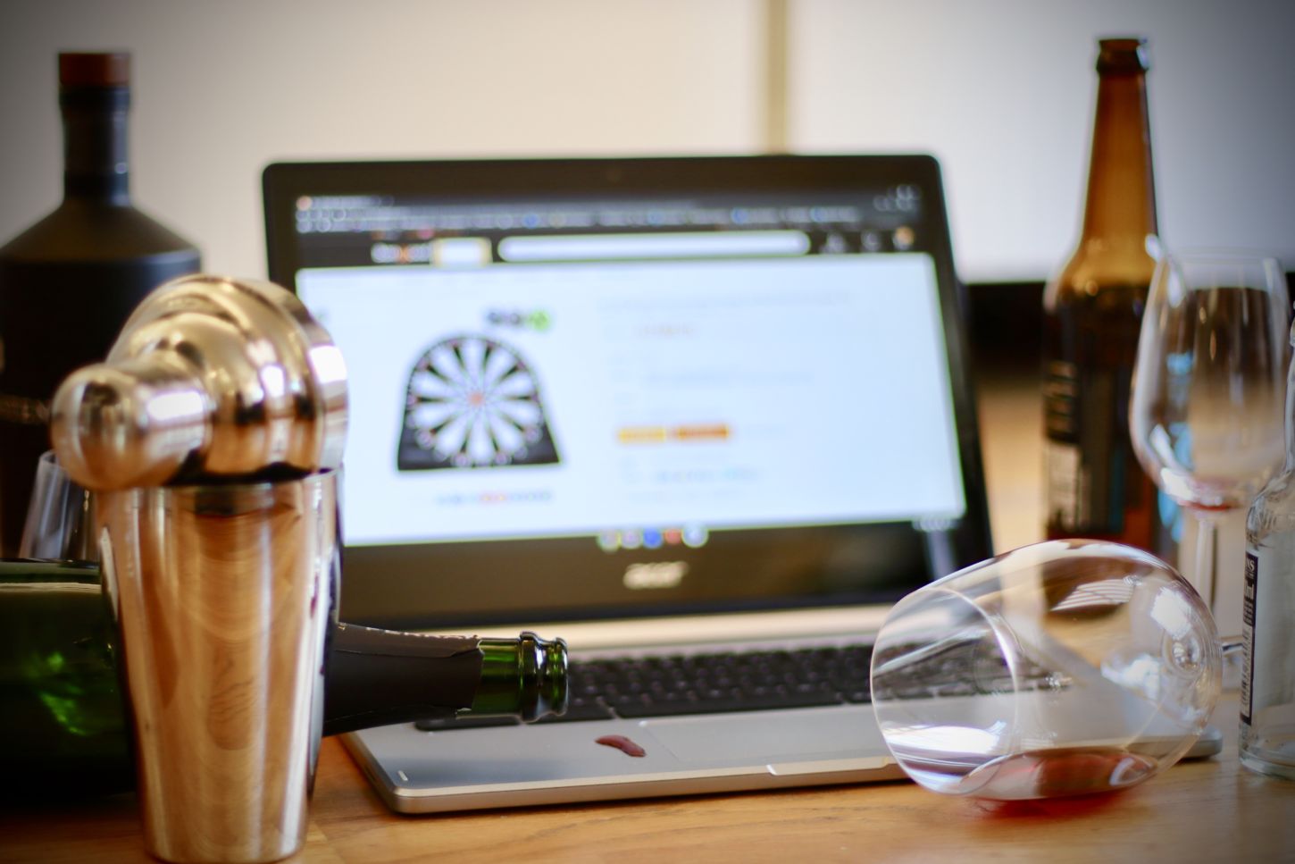Bilde av datamaskin, flasker og veltet glass med vin.