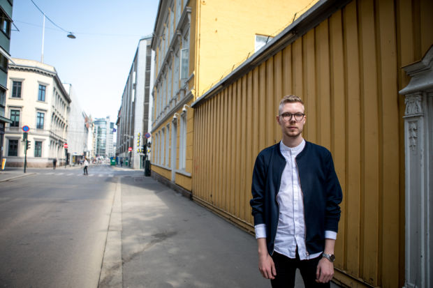 En mann står på et fortau foran et plankegjerde i Oslo Sentrum. Husene i bakgrunnen er gule.