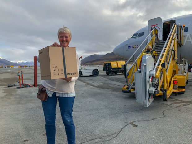 En kvinne står med en pappeske i hånden på vei om bord på et fly. 