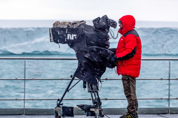 En fotograf står ved et kamera, det blåser og snøen fyker forbi