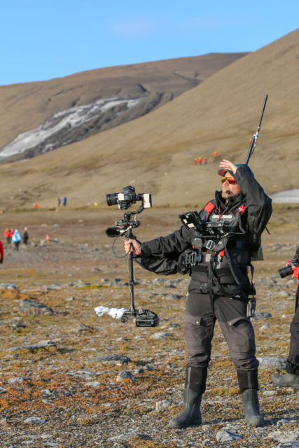 En fotograf med stabiliserende steadicam-rigg på land på Svalbard 