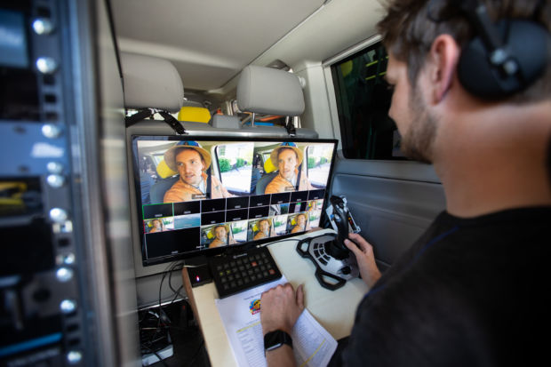 Nærbilde av en person som sitter foran en skjerm med flere bilder på. På en treplate på fanget har personen et ark, en joystick og en kontrollmodul.