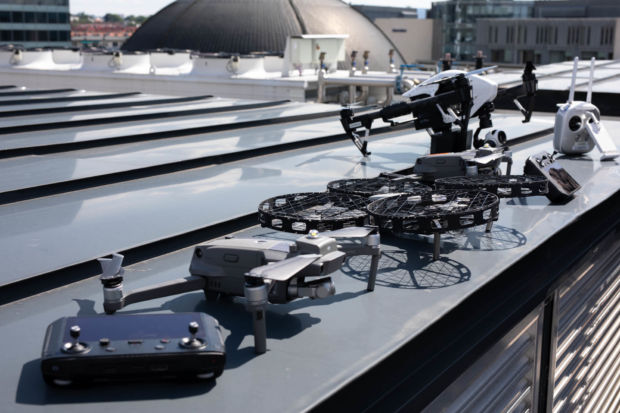 En rekke droner med tilhørende håndkontrollere står utstillt. De fleste er mindre droner, men bakerst skimtes en ganske stor drone av typen DJI Inspire.