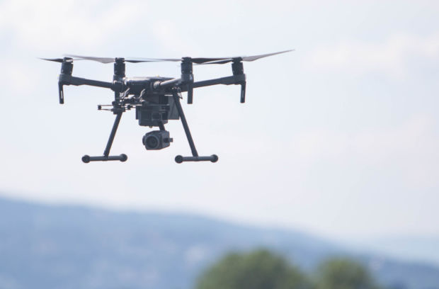 En stor drone av typen DJI Matrice henger i luften. Den er sort og har et kamera hengende under.