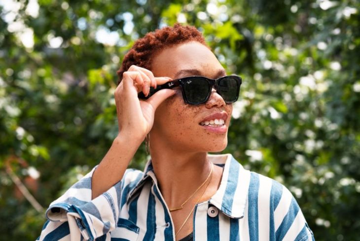 En kvinne har på et par solbriller og trykker med hånden på den ene brillestangen.