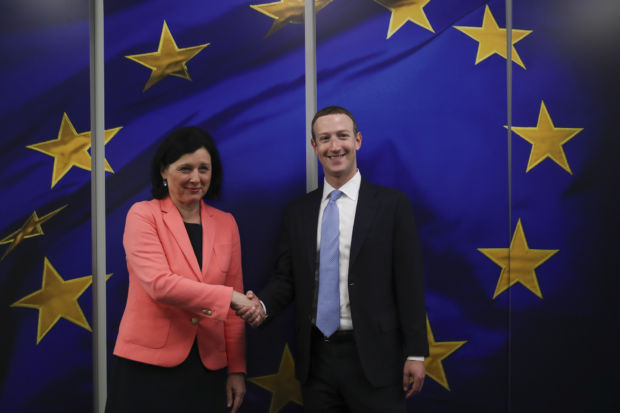 En kvinne og en mann viser et håndtrykk mens de står foran store skjermer som viser EU-flagget.