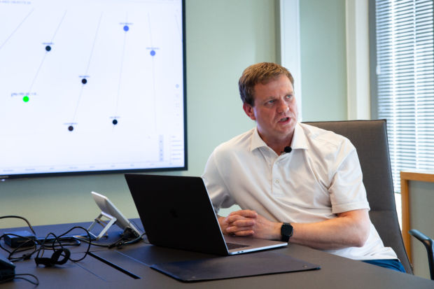 En mann sitter foran en stor skjerm som viser et digitalt nettverk.