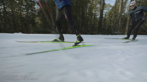 To personer går på ski - begge med ulike sponsor-klær med norske selskaps-logoer.