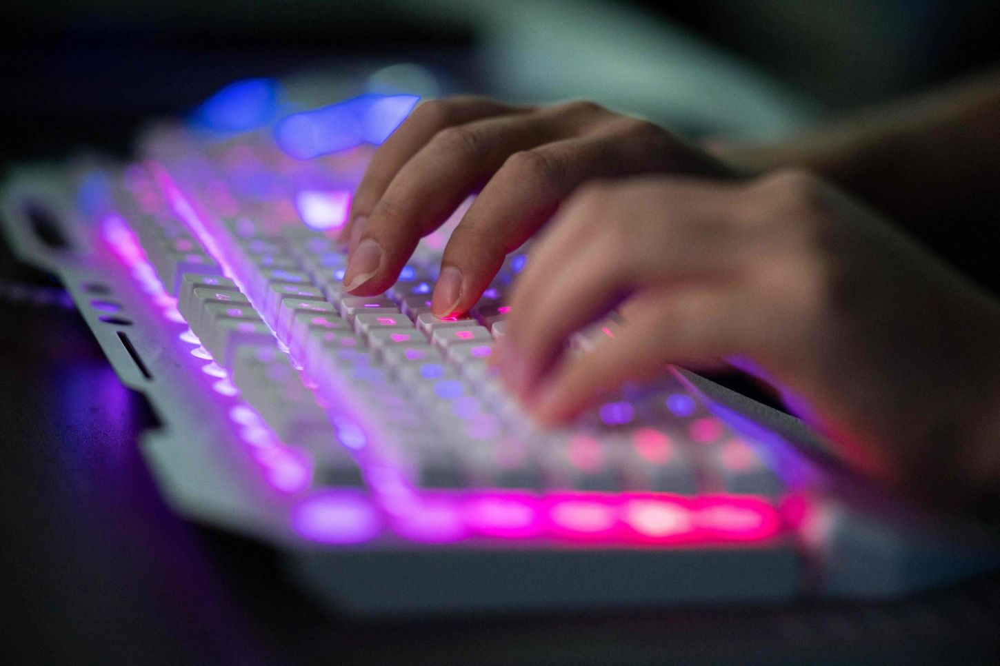To hender på et tastatur som lyser i sterke røde og rosa farger.