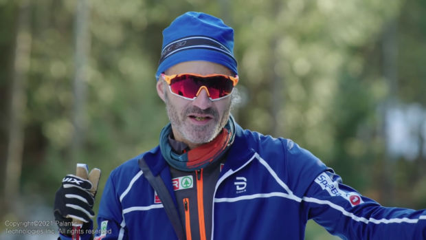 A man in full blue ski gear, with logos of Norwegian companies visible.